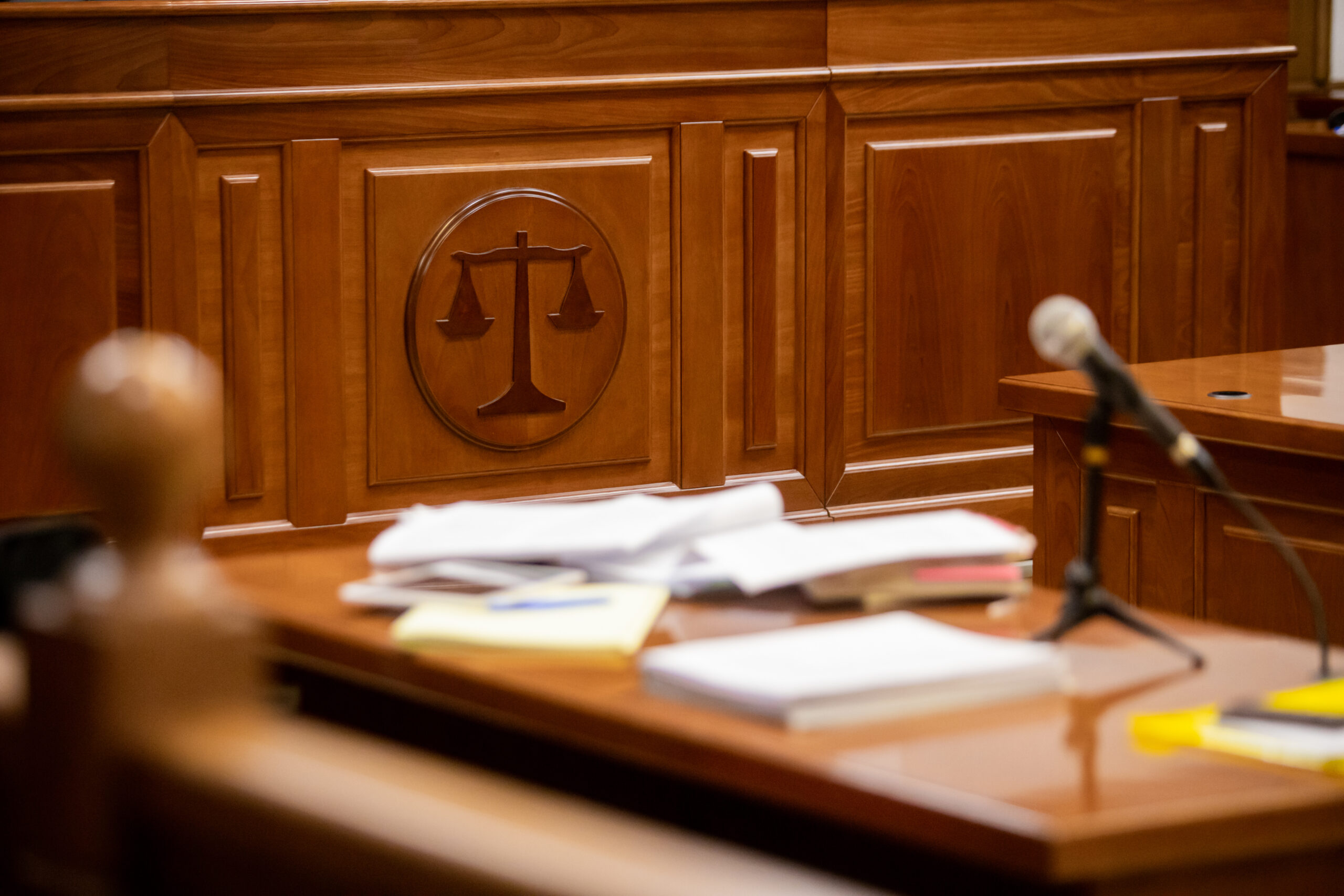 Courtroom table with documents in front of a wooden seal of the scales of justice