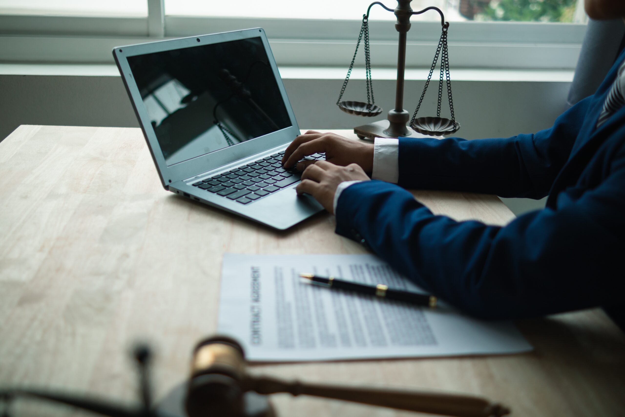 Closeup of an attorney typing on a laptop, with a gavel and scales next to the computer
